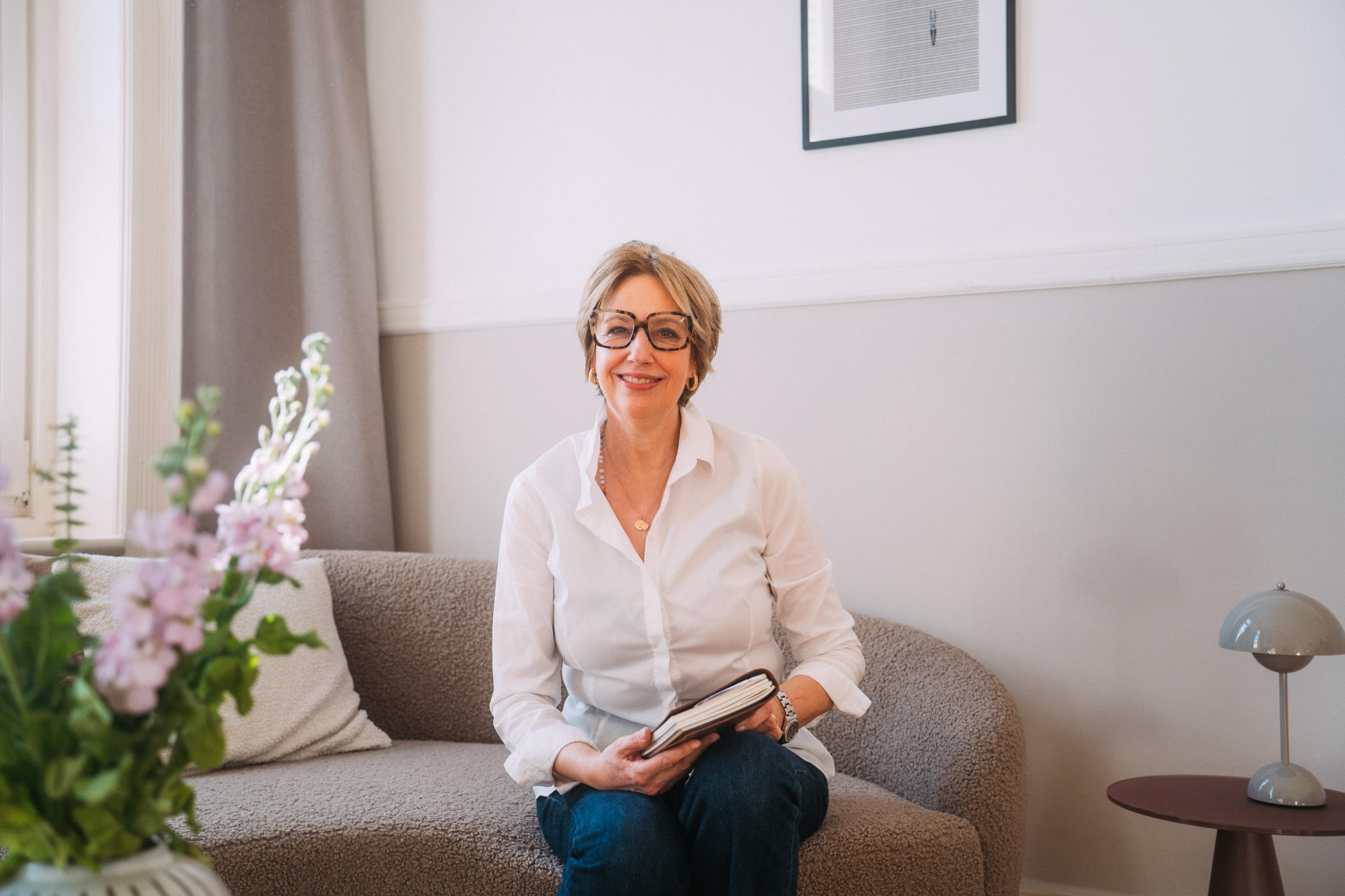 Susanne Moltrecht sitzt lächelnd mit einem Buch auf dem Sofa ihrer Praxis